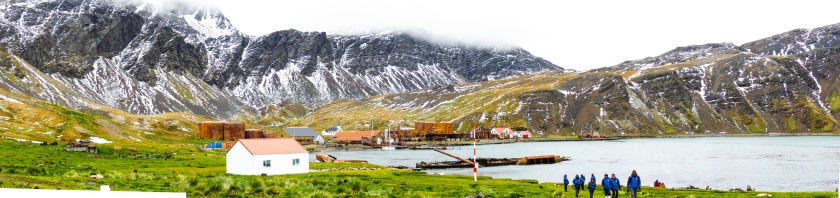 People walking towards Grytviken settlement, which is surrounded by snowy hills