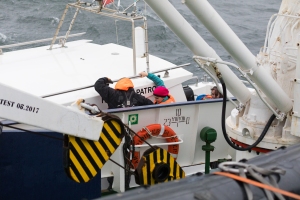Crew member guiding passenger along deck of John Davis pilot ship to board Polar Pioneer 
